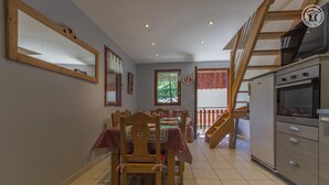 Un comedor con una mesa preparada para cuatro, una silla de madera, una cocina con estufa y una escalera que conduce a un nivel superior.