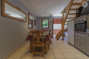 A dining area with a table set for four, a wooden chair, a kitchen with a stove, and a staircase leading to an upper level. - LES IRIS - SAINT SORLIN D'ARVES (SAINT SORLIN D'ARVES)