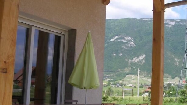 A wooden pergola with a table and chairs, a green umbrella, and a view of a mountainous landscape.
