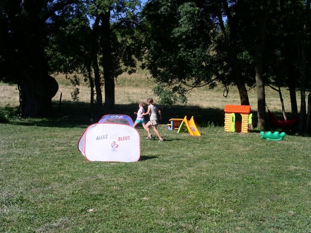 A grassy field with a white inflatable structure labeled "ALLEZ BLEUS" and a small playhouse with a red roof.