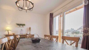 A dining area with a marble table, wooden chairs, a chandelier, and a view through large windows.