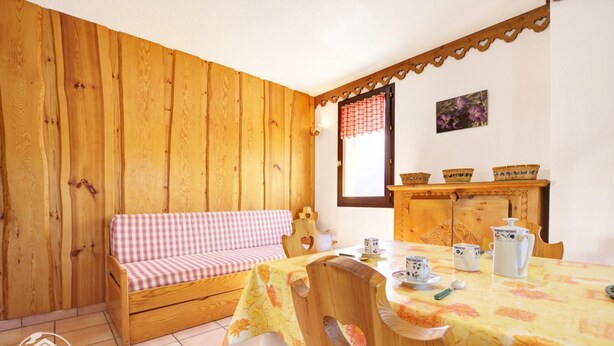 A cozy room with a wooden wall, a checkered sofa, a dining table with floral tablecloth, and a wooden cabinet with baskets. - TRIOLET - AUSSOIS - Gîte (AUSSOIS)