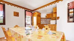 A dining area with a table set for four, wooden chairs, and a view of the outdoors through a window. - TRIOLET - AUSSOIS - Gîte (AUSSOIS)