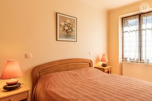 A bedroom with a bed, a nightstand with a lamp, a wall-mounted picture, and a window with curtains. - MUSCARIS - AIX LES BAINS (AIX LES BAINS)
