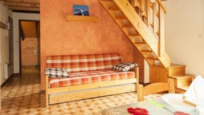 Um quarto acolhedor com uma escada de madeira, um sofá xadrez e uma pequena mesa com um prato e guardanapo.