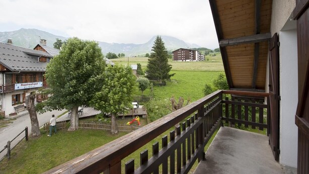 Uma varanda com vista para uma paisagem rural, incluindo um restaurante, uma grande árvore e montanhas ao longe.