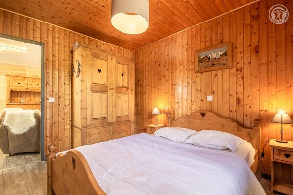 Una habitación de madera con una cama, dos mesitas de noche con lámparas, un armario y un cuadro en la pared.