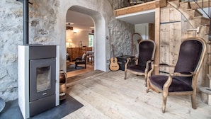 A rustic interior with a stone wall, a fireplace, wooden furniture, and a balcony.