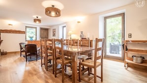 A dining area with a wooden table and chairs, pendant lights, and a view of the outdoors through large windows.