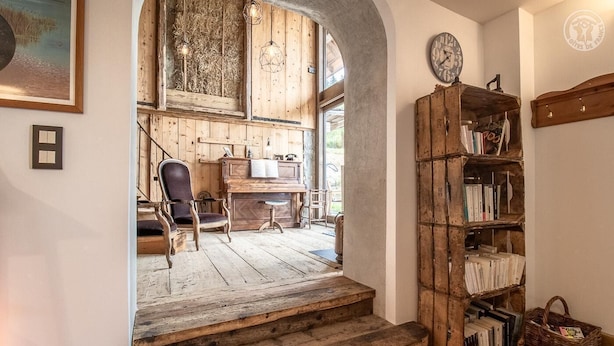 A rustic interior with wooden floors, a piano, a bookshelf, and a large clock on the wall.