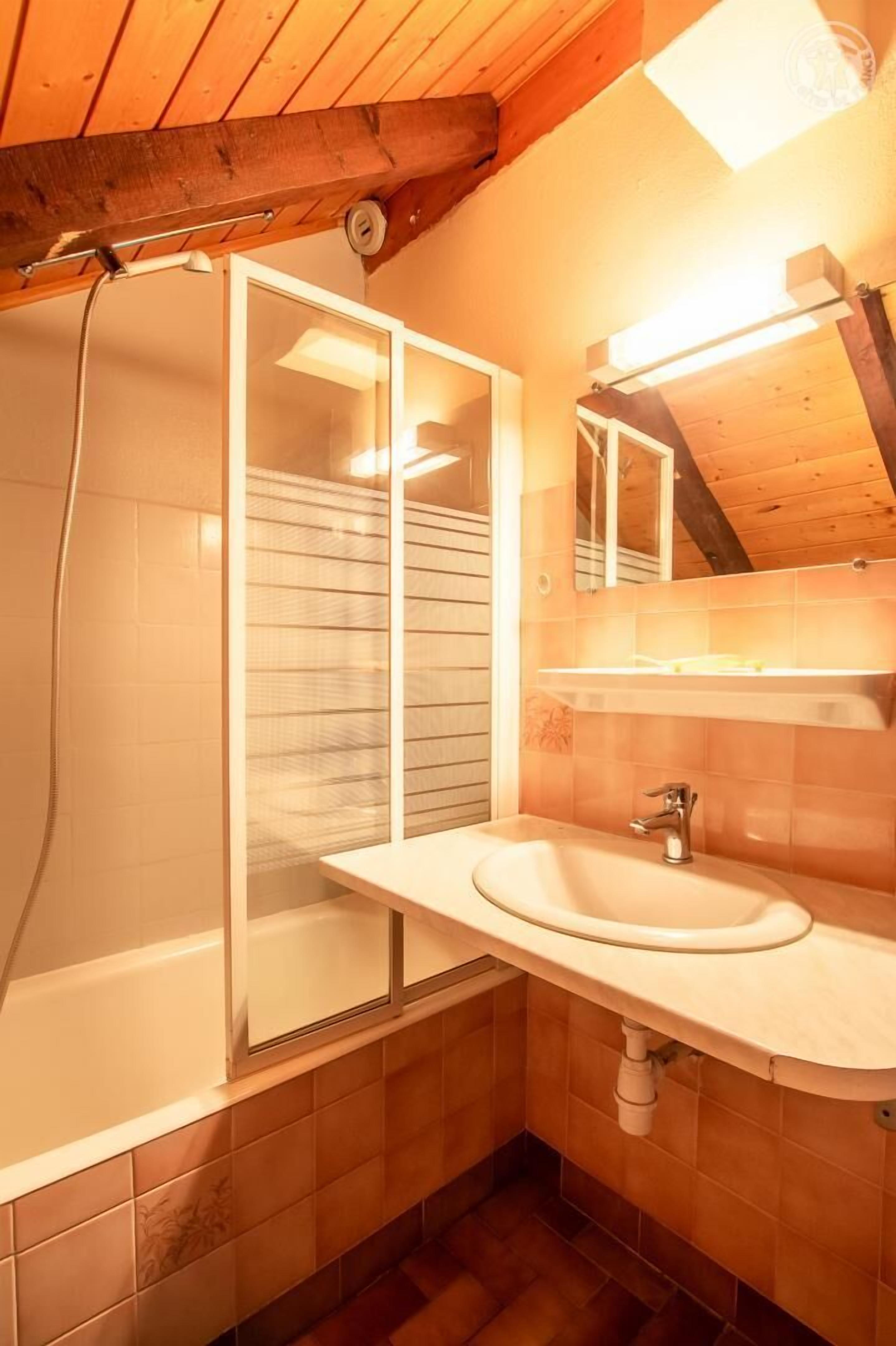 A bathroom with a wooden ceiling, a bathtub, a sink, and a mirror.