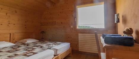 Habitación de cabaña de madera con dos camas, una mesa, una silla, un ventanal y un radiador.