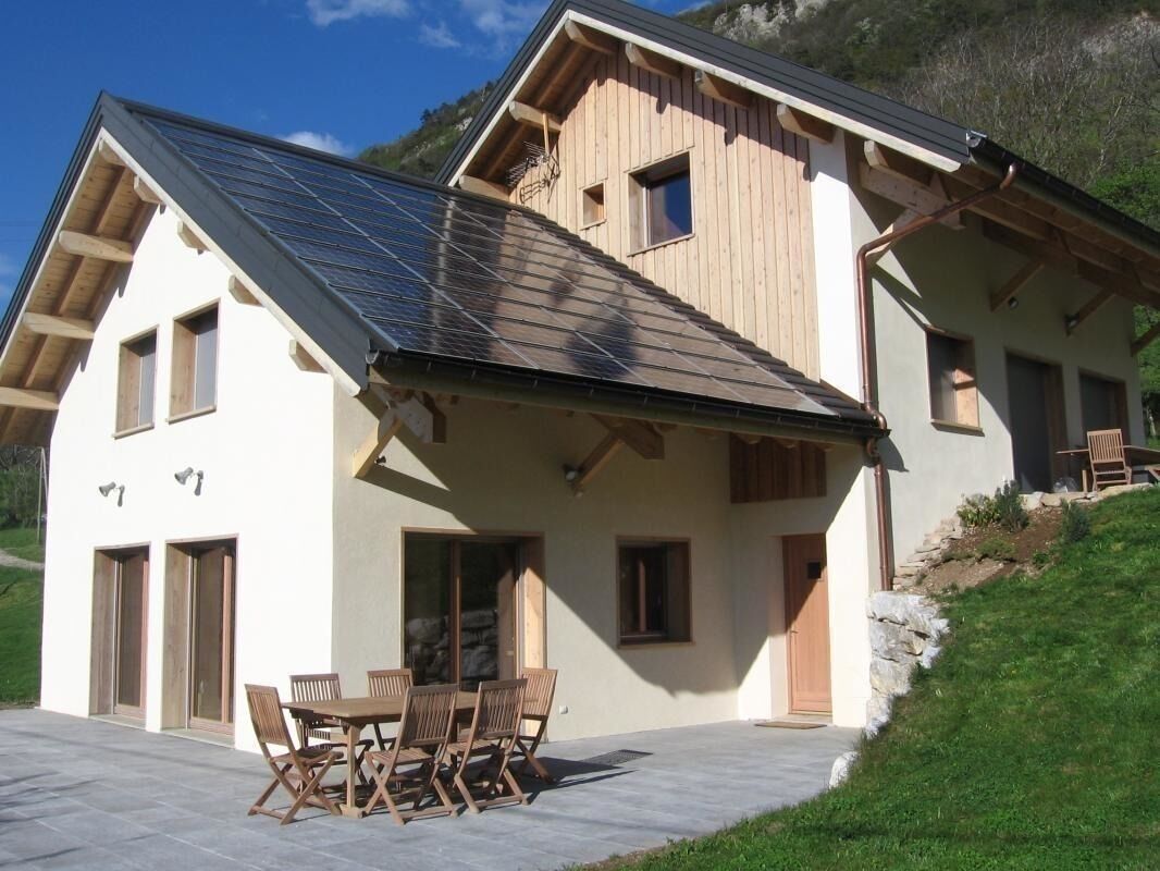 Una casa de dos pisos con techo inclinado, fachada de madera y un patio con mesa y sillas.