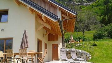 A modern house with a patio, wooden furniture, and a stone wall.