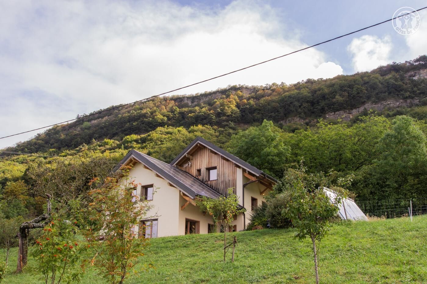 Une maison à deux étages, dotée d’un toit en pente, entourée d’une pelouse et d’arbres.