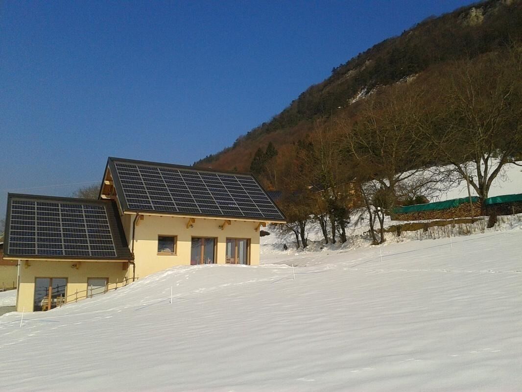 Une maison dotée de panneaux solaires sur le toit, située sur une colline enneigée.