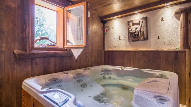 A wooden cabin interior with a hot tub, wooden walls, a window with a view of trees, and a ski-themed decoration on the wall. - LE PAMYDA - HAUTELUCE LES SAISIES (HAUTELUCE LES SAISIES)