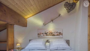 A cozy bedroom with a wooden ceiling, a bed with checkered bedding, a nightstand with a lamp, and a wall-mounted light fixture. - LE PAMYDA - HAUTELUCE LES SAISIES (HAUTELUCE LES SAISIES)