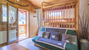 A cozy wooden cabin interior with a green sofa, a wooden ceiling, and a view of the outdoors through a glass door. - LE PAMYDA - HAUTELUCE LES SAISIES (HAUTELUCE LES SAISIES)