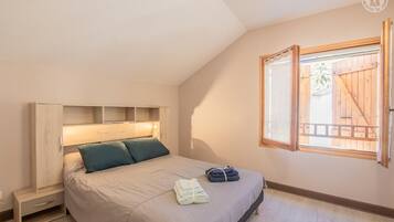 Ein Schlafzimmer mit einem Bett, einem Holz-Kopfteil, einem Fenster mit geöffnetem Rollo und einem kleinen Nachttisch.