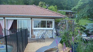 A wooden deck with a stone wall, a lounge chair, and a small table.