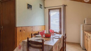 A dining area with a wooden table set for two, a window with curtains, and a kitchenette with a microwave. - LE BARBIER - AUSSOIS (AUSSOIS)