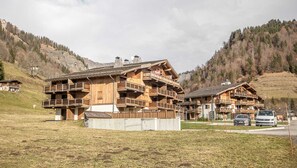 Situated on a grassy slope, this chalet-style building offers a serene mountain setting with multiple balconies and a steeply pitched roof.