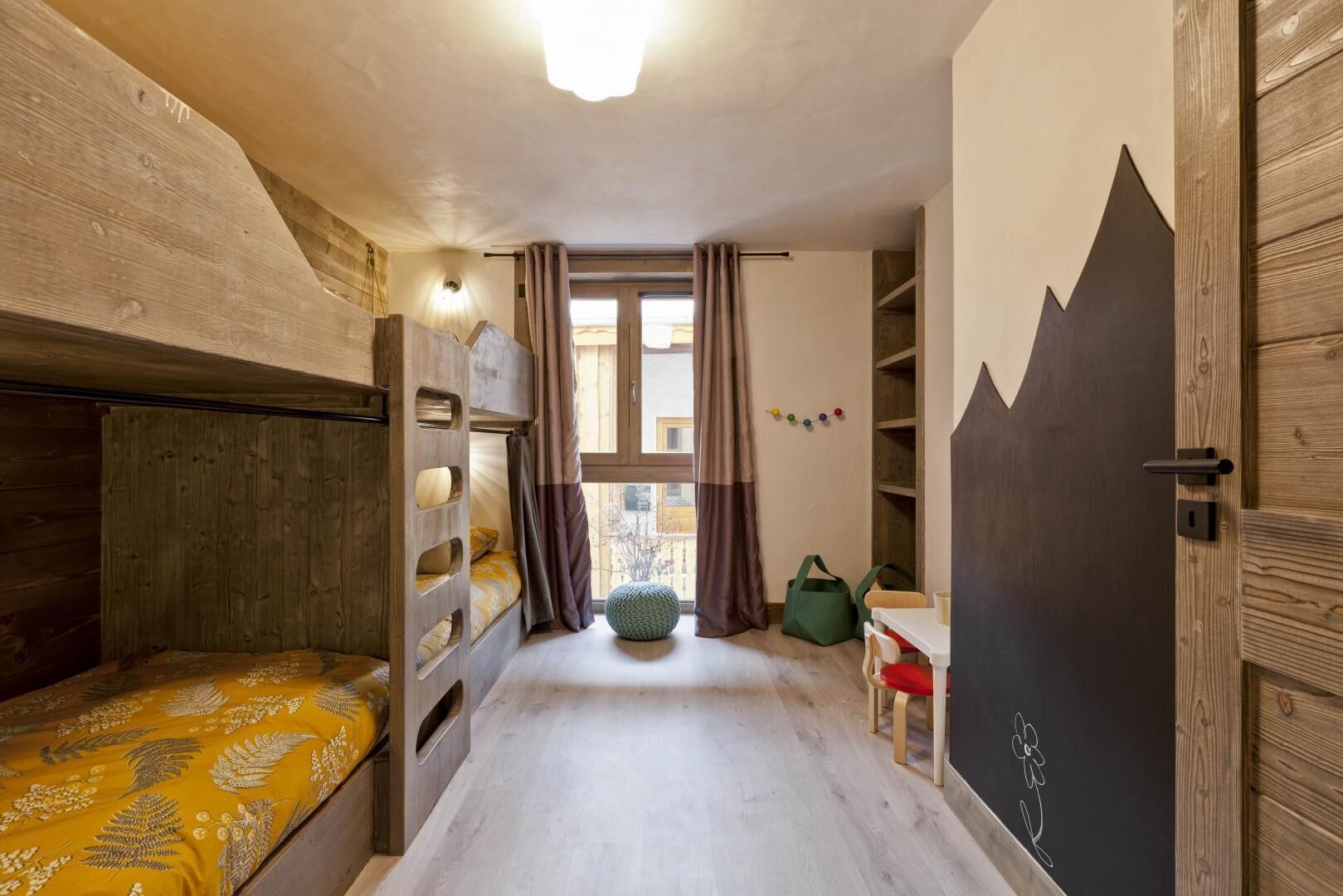 A cozy room with bunk beds, a small table, a chair, and a window with curtains.