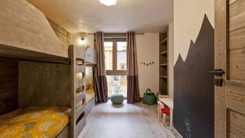 A cozy room with bunk beds, a small table, a chair, and a window with curtains.