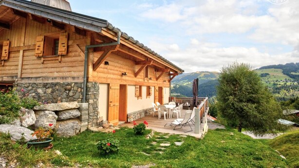 Eine Holzhütte mit Steinfundament, einer Veranda mit Sitzgelegenheit und Blick auf eine schöne Berglandschaft.
