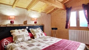 Ein gemütliches Schlafzimmer in einer Holzhütte mit einem Bett, zwei Wandlampen, einem Fenster mit Vorhängen und einer Heizung.