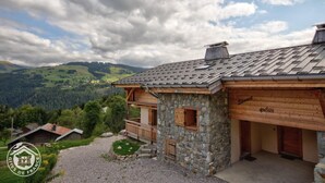 Ein Steinhaus mit einem hölzernen Balkon, einer Garage und Blick auf eine gebirgige Landschaft.