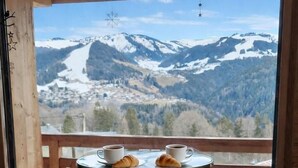 Ein Holzbalkon mit Tisch und zwei Stühlen, mit Blick auf eine Berglandschaft.