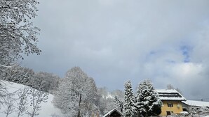 A snow-covered landscape with a yellow building, a wooden cabin, and a road.