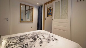 A bedroom with a bed featuring a large animal print, a mirror, a door with frosted glass panels, and a wall-mounted light fixture.