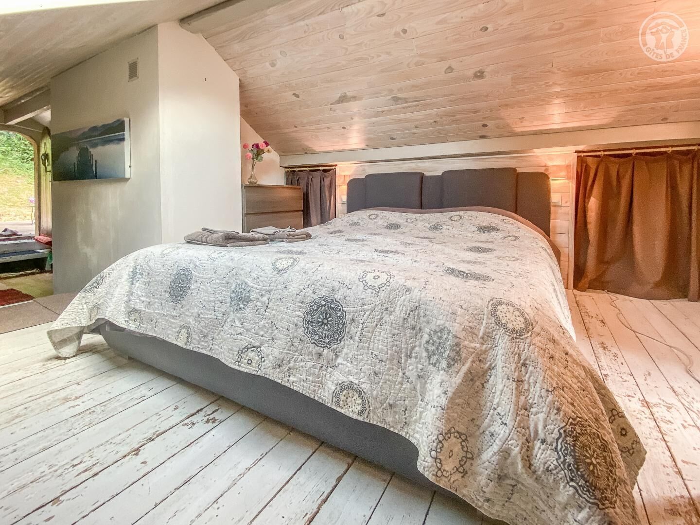 A bedroom with a large bed, wooden ceiling, and a view of the outdoors.
