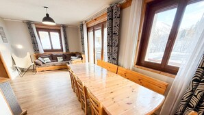 Ein gemütliches Zimmer mit Holztisch, Stühlen, einer Couch und einem Fenster mit Vorhängen.