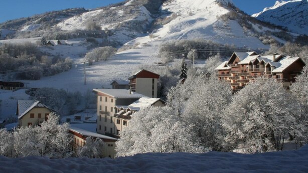 Ein schneebedeckter Berg mit einem Skiort im Vordergrund, mit Chalets und blauem Himmel.