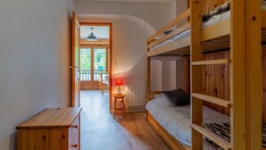 Ein Zimmer mit Etagenbetten, einer Holzkommode, einer Lampe und Balkonblick.