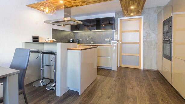 A modern kitchen with a central island, stainless steel appliances, and a wooden ceiling.