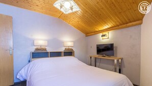 A bedroom with a wooden ceiling, a bed with white bedding, two bedside lamps, a TV on a wooden stand, and a door on the left.