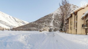 A snow-covered road leading to a building with a mountain backdrop.