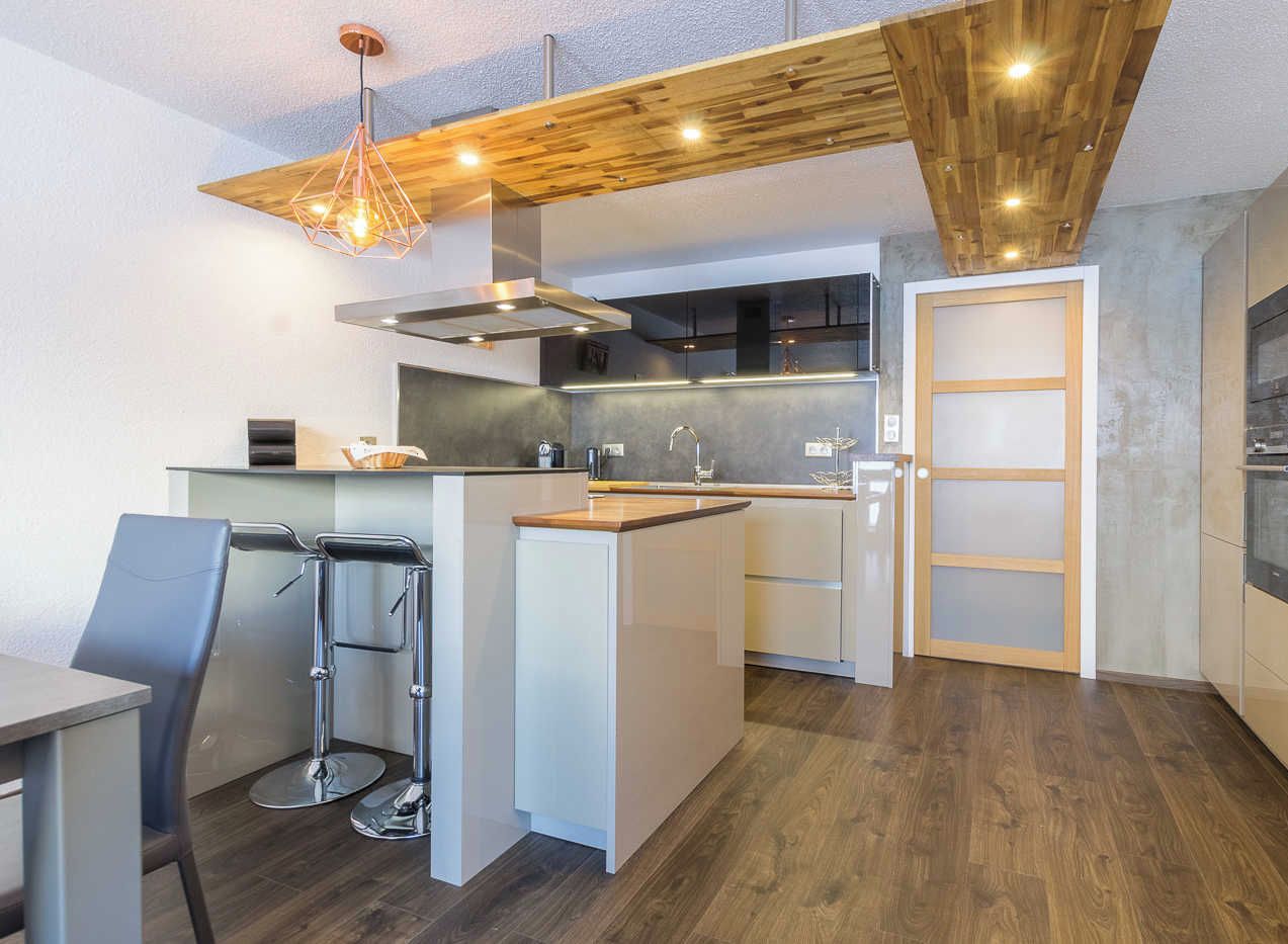 A modern kitchen with a central island, stainless steel appliances, and a wooden ceiling.