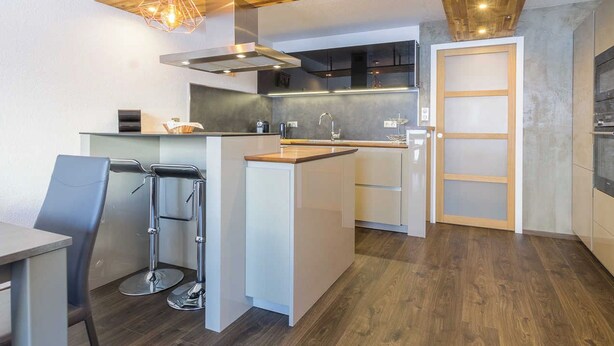 Eine moderne Küche mit einer zentralen Kochinsel, Edelstahlgeräten und einer Holzbalkendecke.