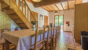 Un comedor con una larga mesa de madera y sillas, una escalera y vistas al exterior.