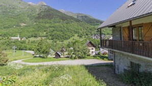 Un pueblo de montaña con casas de madera tradicionales, un edificio de piedra con balcón y una vista despejada de las colinas circundantes.