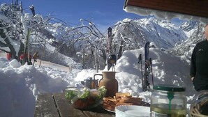 Una mesa de madera con comida, bebidas, una botella y vistas de montañas nevadas y equipo de esquí.