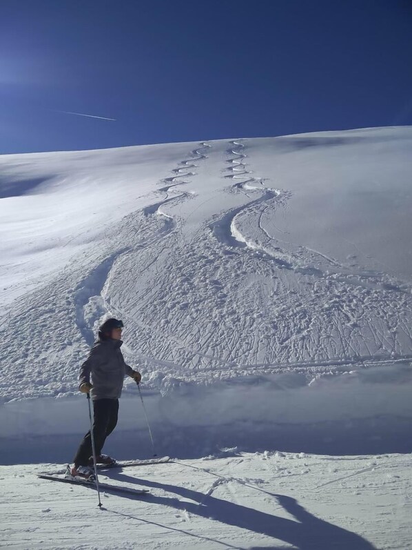 Eine Person fährt Ski auf einem verschneiten Hang, deutliche Spuren im Schnee sind sichtbar.