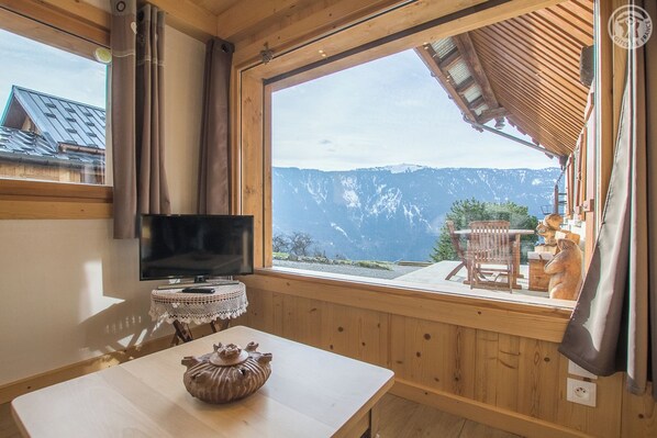 A room with a television, a table with a decorative item, and a view of mountains through a large window.