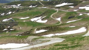 Una carretera sinuosa de montaña con parches de nieve y hierba verde.